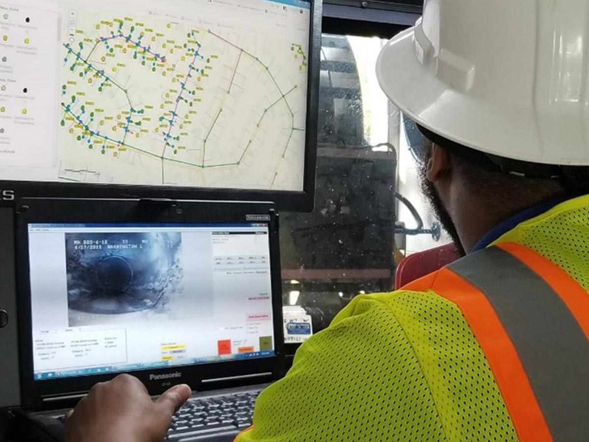 A Hydromax USA worker monitoring video from inside a pipeline and a utility map side-by-side.