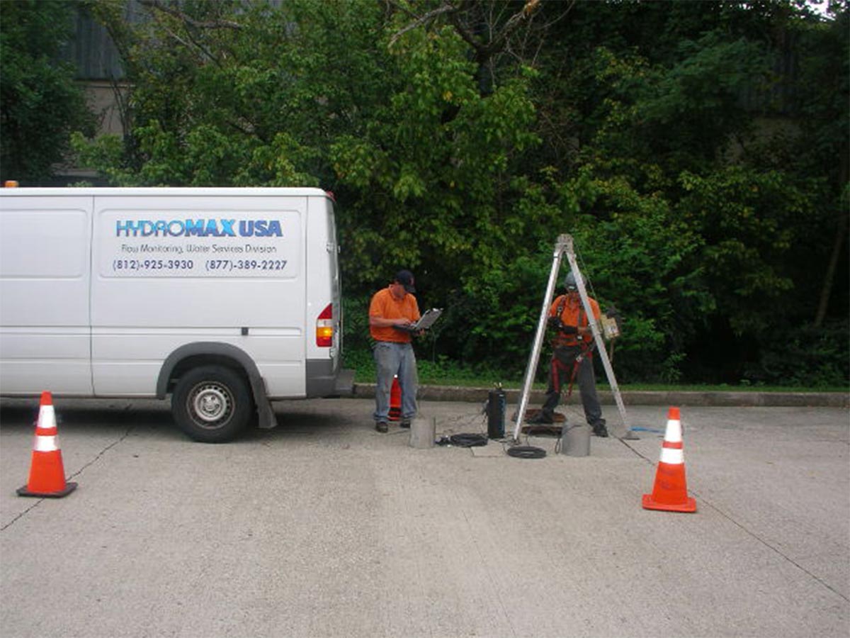 Two HydroMax USA employees working over a manhole, preparing to install a Flow Monitor.