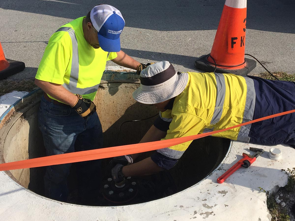 Two Hydromax USA workers working in a shallow manhole that has been cordoned off for safety.