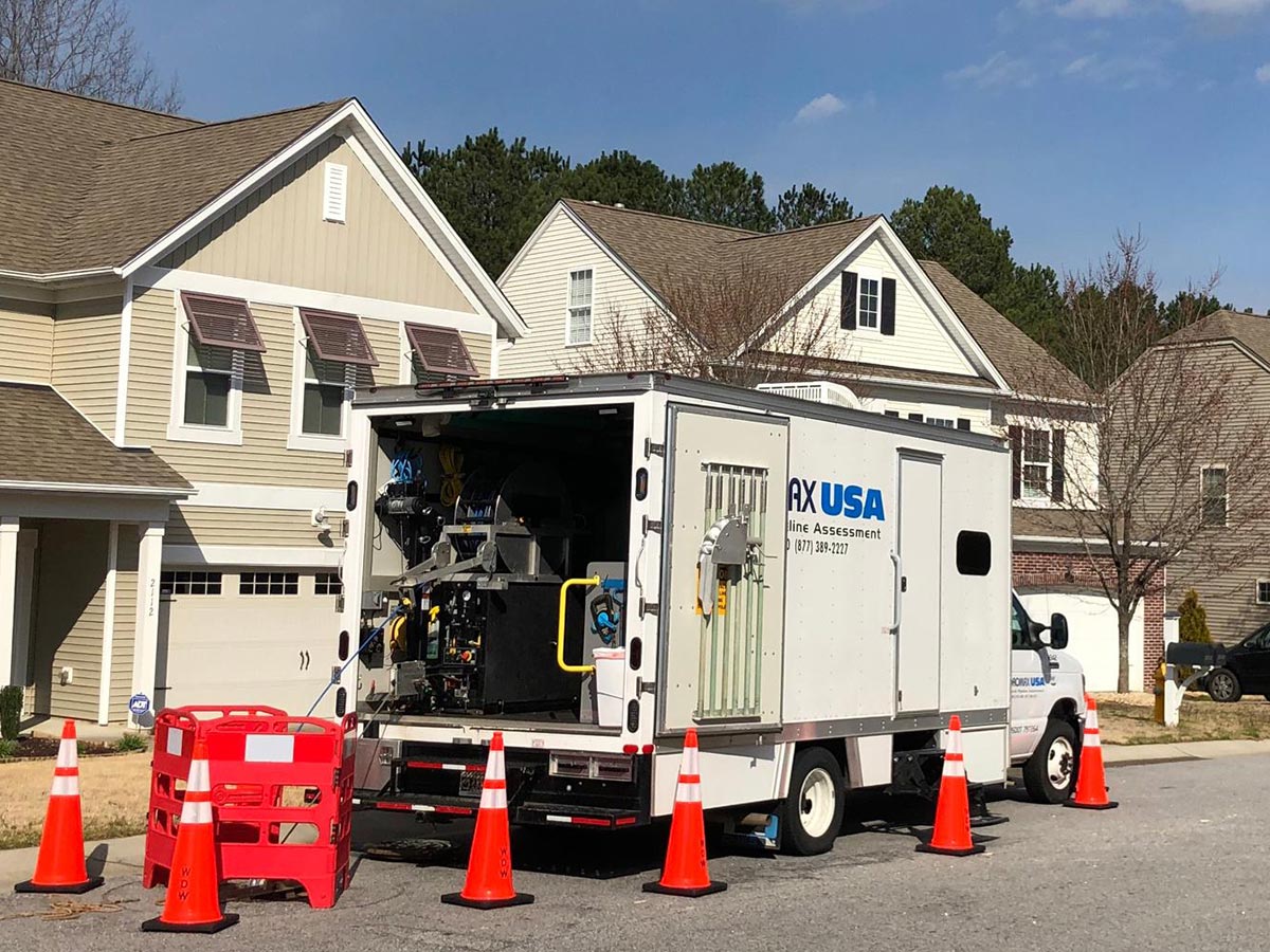 A Hydromax USA CCTV inspection truck parked on a street by a manhole, surrounded by safety cones.