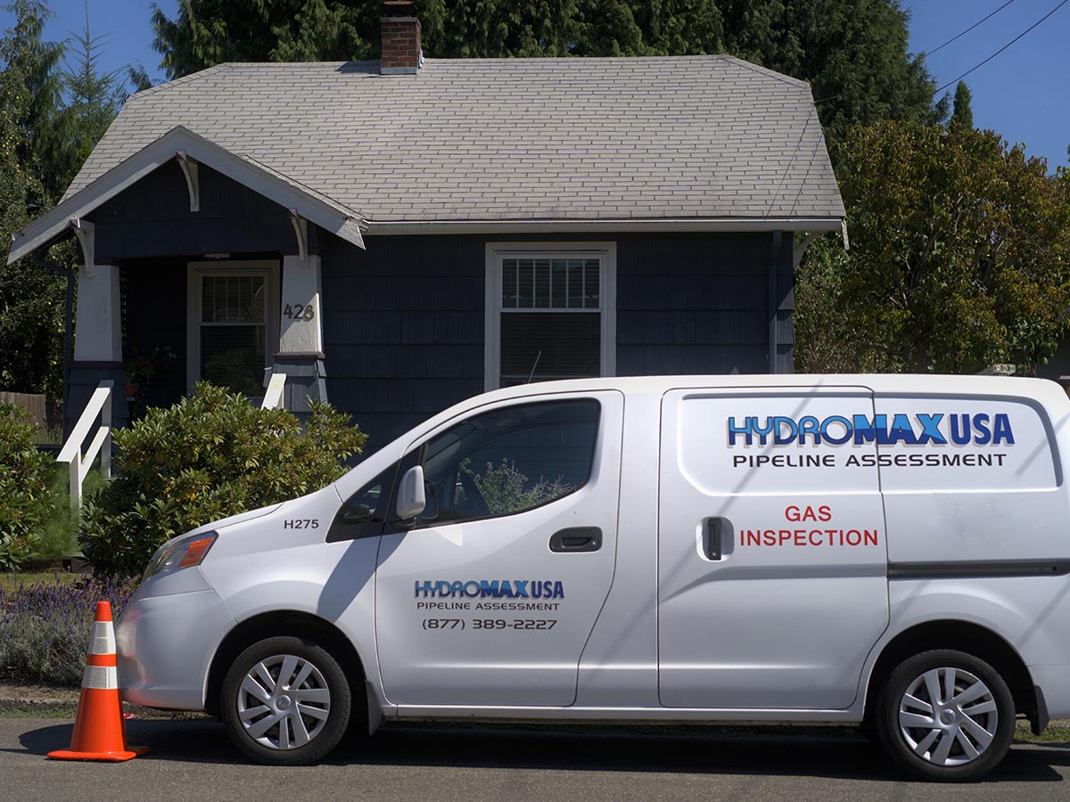 A Hydromax USA gas inspection van parked in front of a house.